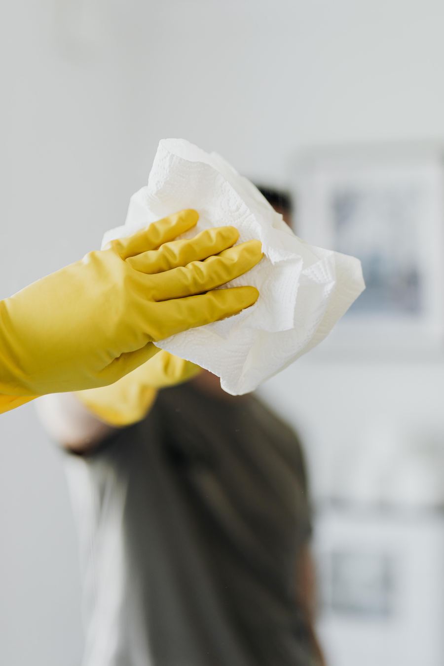 A caregiver wearing cleaning gloves wiping down a surface with a paper towel