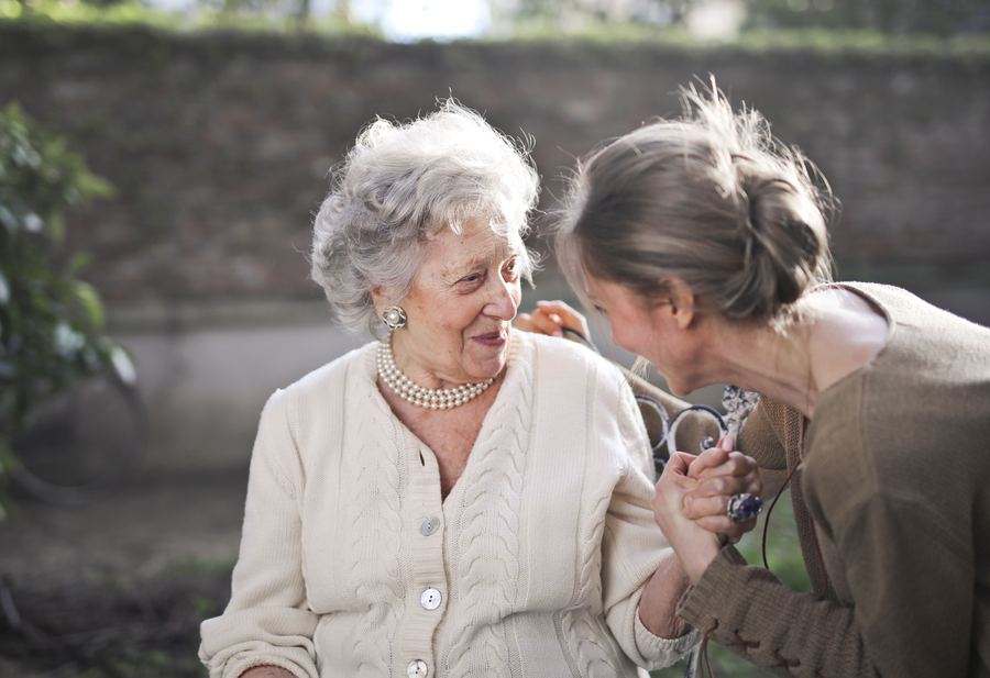 An older woman warmly holding hands with a younger caregiver outdoors